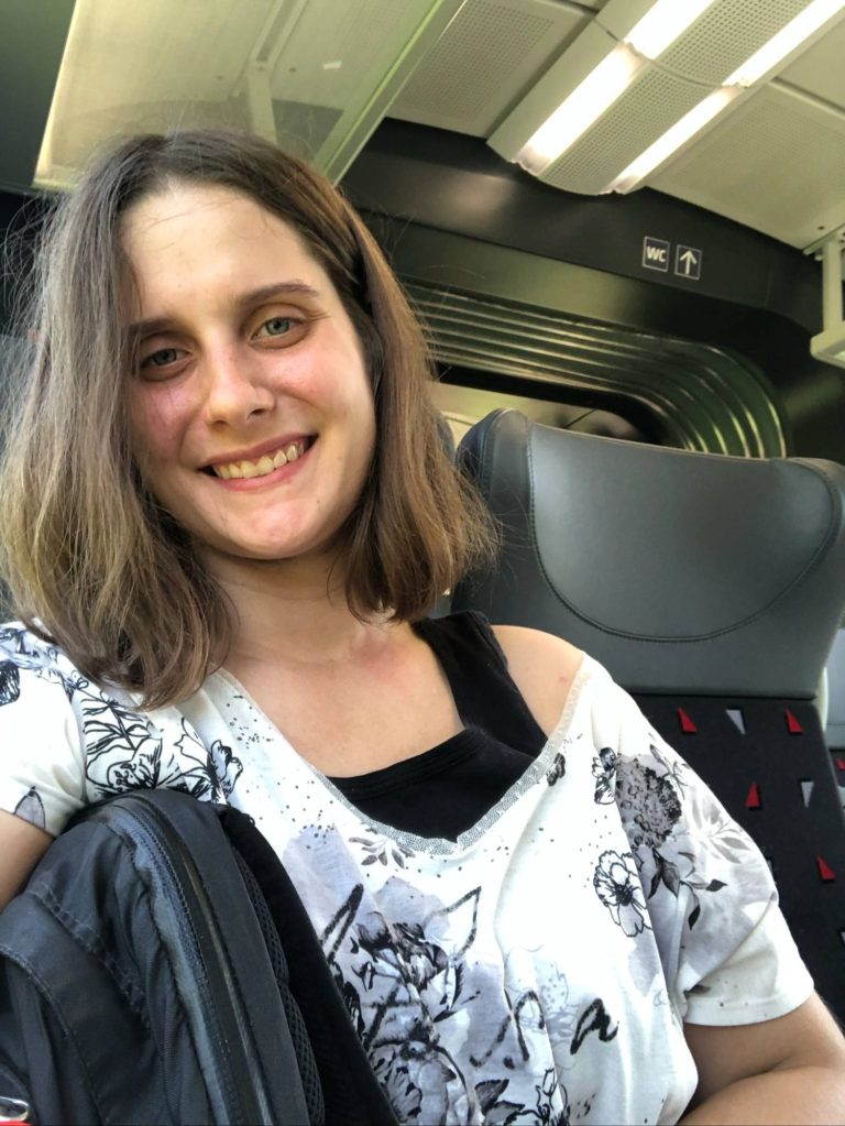 Junge Frau mit lässigem Outfit lächelt in einem Zugabteil.