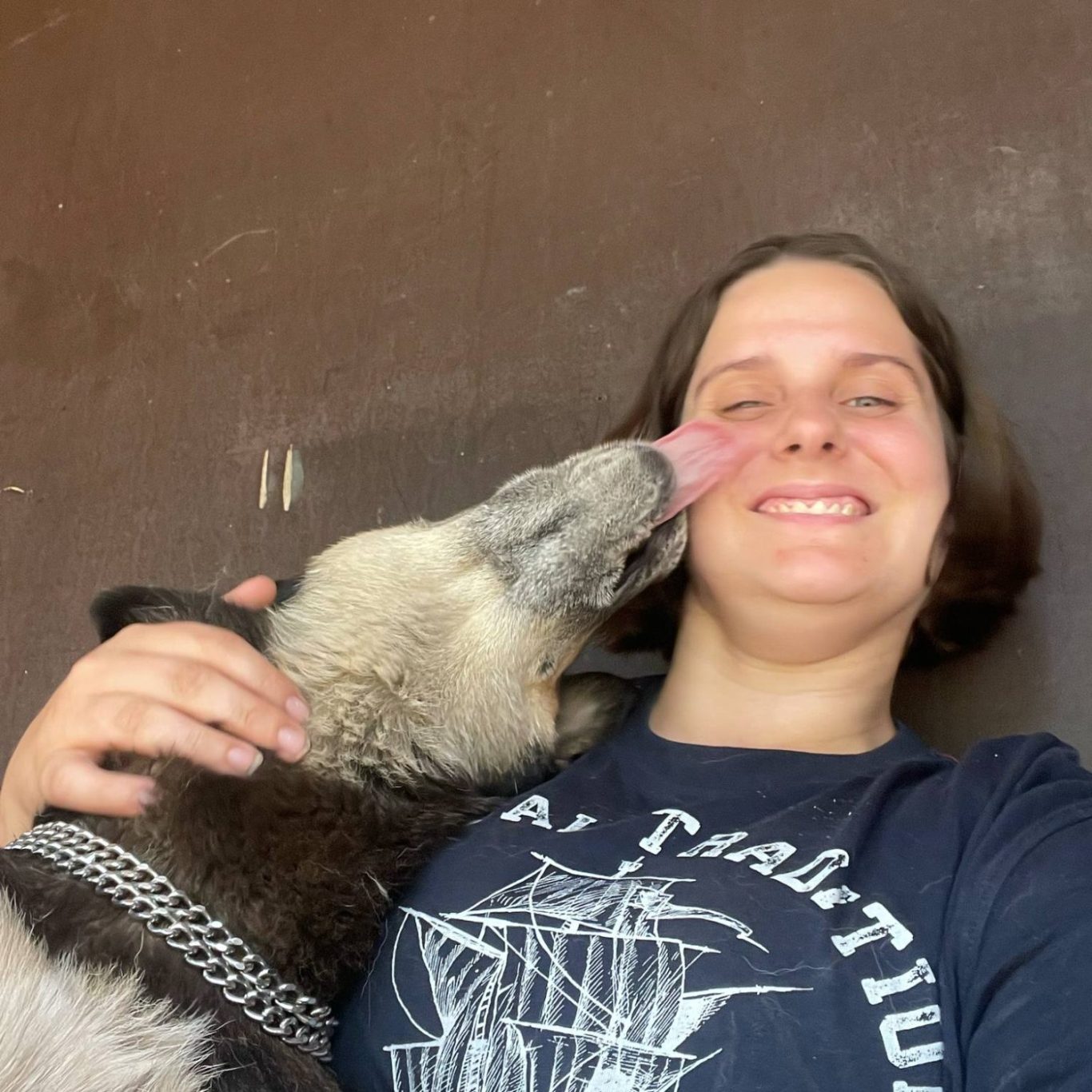 Frau mit kurzen Haaren lächelt, während ein Hund ihr Gesicht leckt.