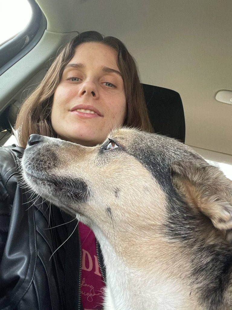 Hund mit Maulkorb steht auf Gras, schaut direkt in die Kamera.