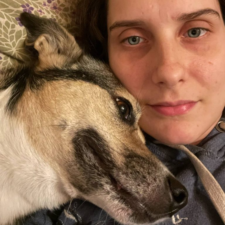 Frau liegt neben einem Hund, beide schauen entspannt in die Kamera.